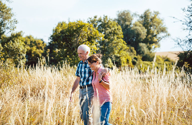 Une femme et un homme marchent bras dessus bras dessous dans une prairie. 